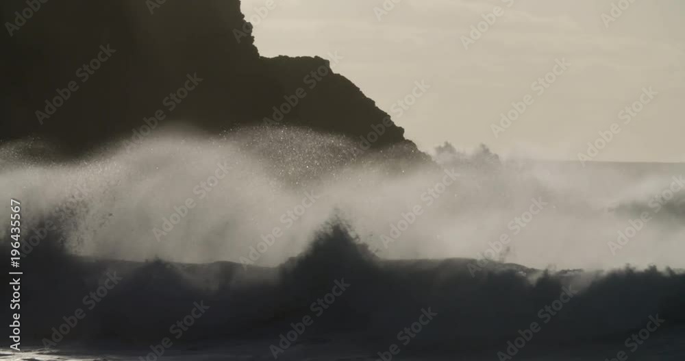 Blue waves roll into the coast of Hawaii and crash into the shore in slow motion during a big storm.