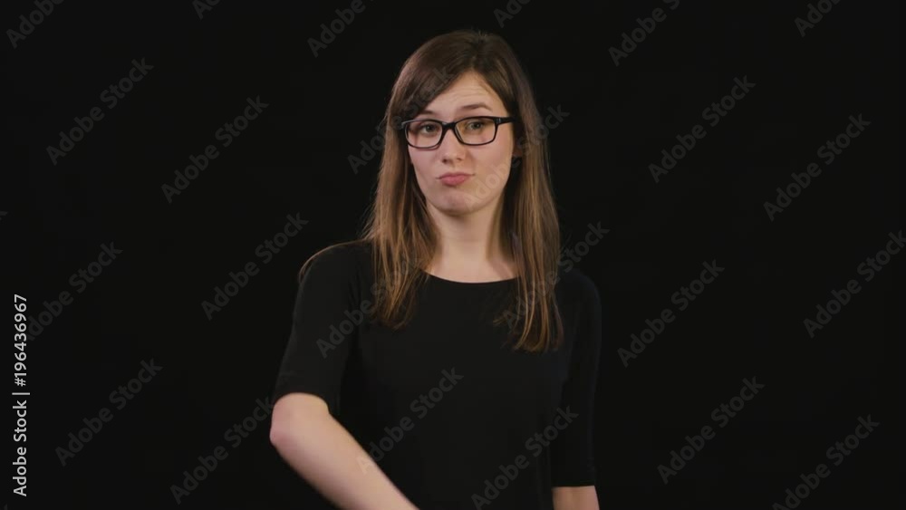 A beautiful young lady touches her black glasses with her finger against a black background. Medium Shot A beautiful young lady touches her black glasses with her finger against a black background. Medium Shot