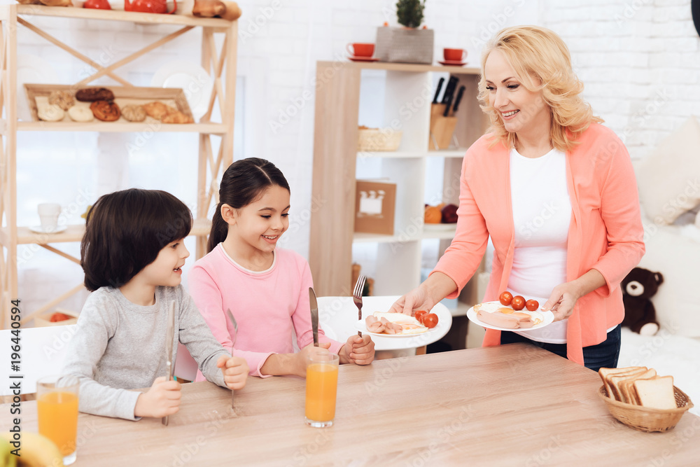 Little grandchildren sit in kitchen and wait for beautiful grandmother to bring dinner. Little grandchildren sit in kitchen and wait for beautiful grandmother to bring dinner.