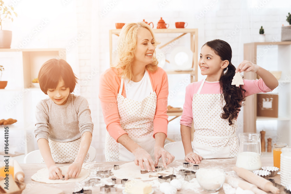Beautiful grandmother in her apron together with her little grandsons cooks cookies in kitchen. Beautiful grandmother in her apron together with her little grandsons cooks cookies in kitchen.