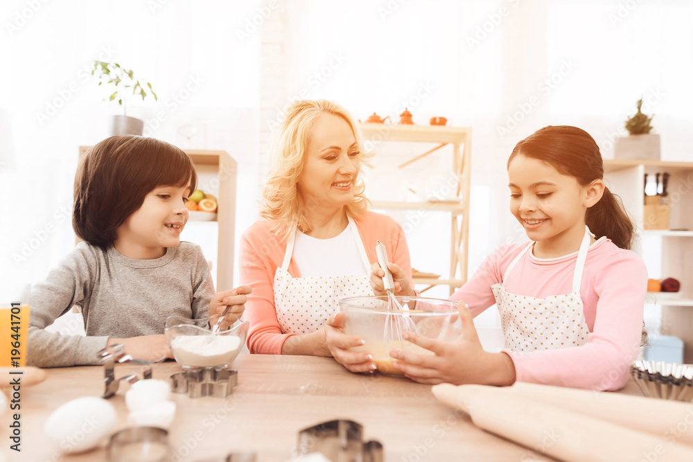 Joyful little girl is beating eggs in bowl with milk and her brother is pouring flour. Joyful little girl is beating eggs in bowl with milk and her brother is pouring flour.