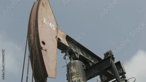 An oil pump-jack rises and falls as clouds pass across a blue sky in time lapse.