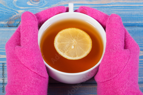 Hand of woman in gloves holding cup of hot tea on table