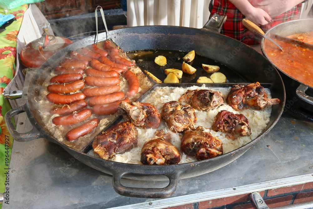 Fast street-food - smoked pork sausages, chicken legs and stewed cabbage with popato in big frying pan. Fast street-food - smoked pork sausages, chicken legs and stewed cabbage with popato in big frying pan.