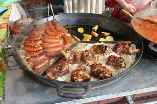 Fast street-food - smoked pork sausages, chicken legs and stewed cabbage with popato in big frying pan.