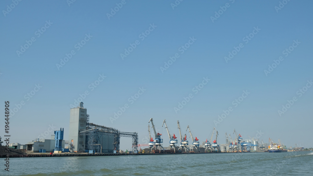 river port with cranes and industrial buildings in summer against a blue clear sky view from the water