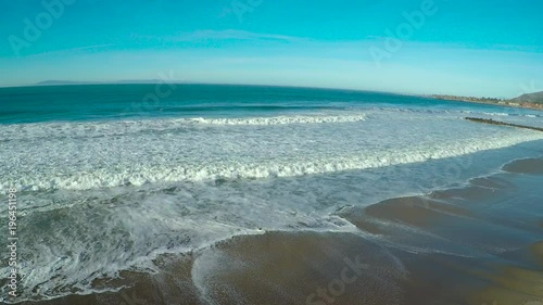 An aerial over a generic beach heading out to the ocean with large waves and surf breaking.