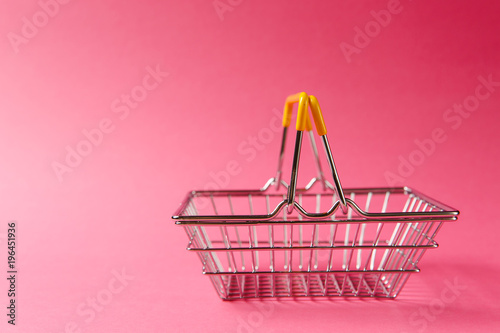 Close up of metal grocery basket for shopping in supermarket with raised handles and yellow plastic elements isolated on pink background. Concept of shopping. Copy space for advertisement