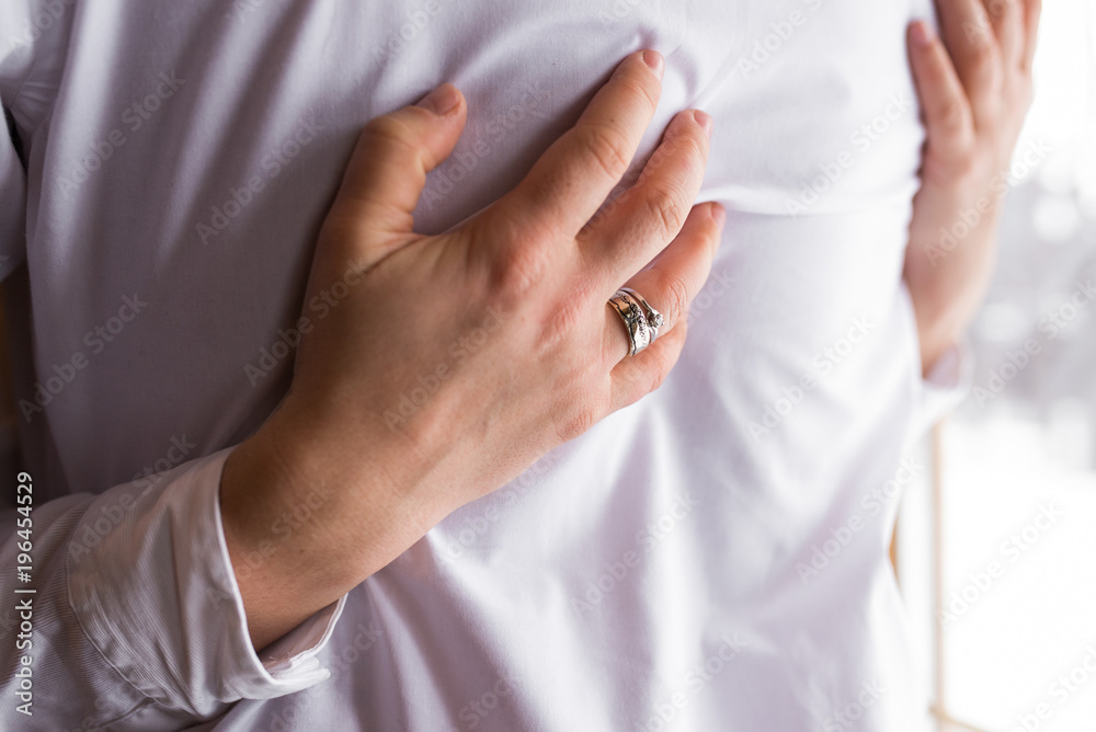 Silver wedding ring and engagement ring with diamond on hand of woman. Bride hugging the groom in suit