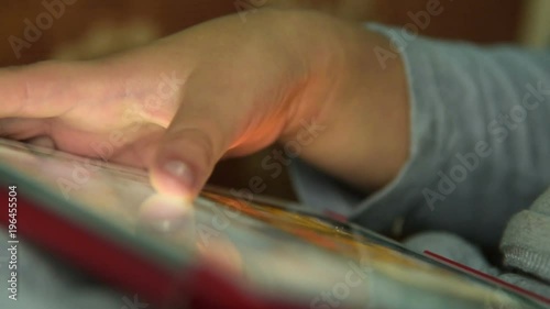 Close-up shot of little kid playing game on digital tablet, fingers moving on touchscreen