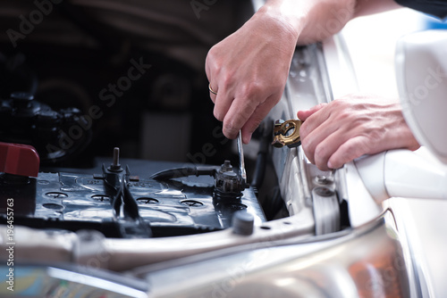 Action of man hands using spanner remove car battery terminals to change the new one, car fixing and maintenance service concept.