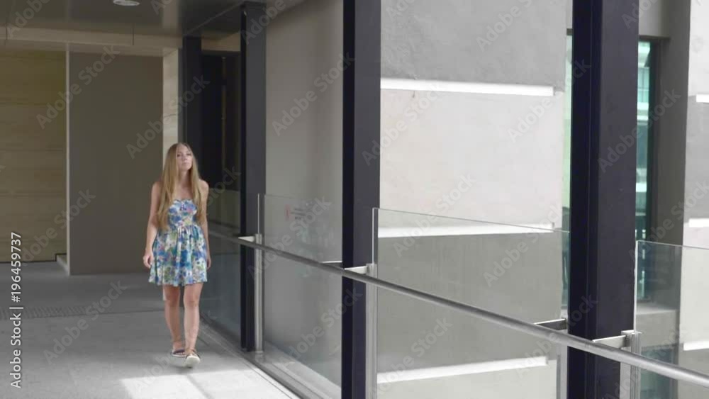 Young attractive woman in colorful summer dress walking along hte hall in business center. Young attractive woman in colorful summer dress walking along hte hall in business center.