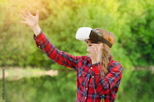 Girl in the helmet of virtual reality against the background of nature. Hands up
