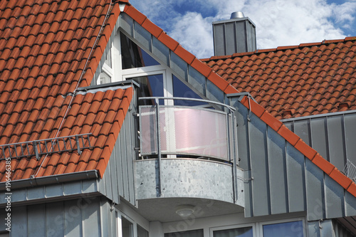 Moderner Metall-Balkon, integriert in ein Ziegeldach mit rostfreier Stehfalz-Metall-Verkleidung des seitlichen Dach-Abschlusses