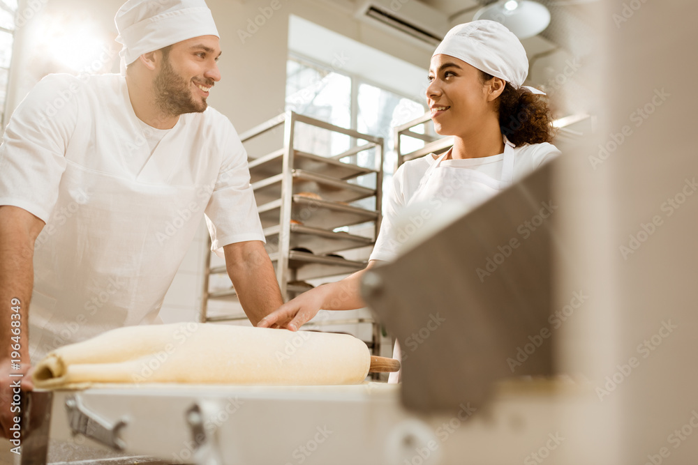 happy young bakers working with industrial dough roller at baking manufacture happy young bakers working with industrial dough roller at baking manufacture