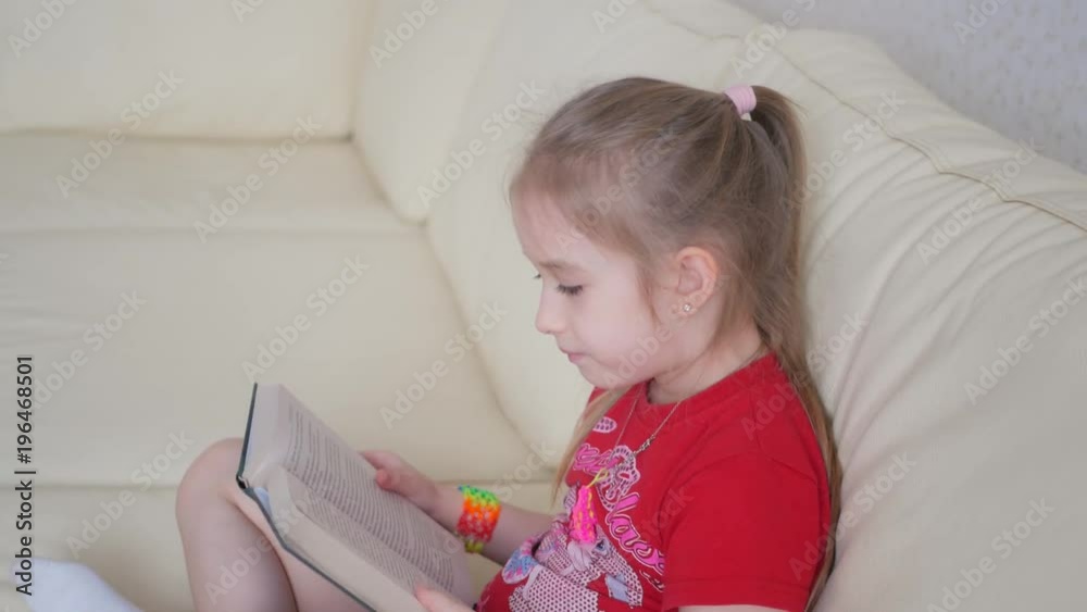 Charming little girl reading book on sofa Charming little girl reading book on sofa