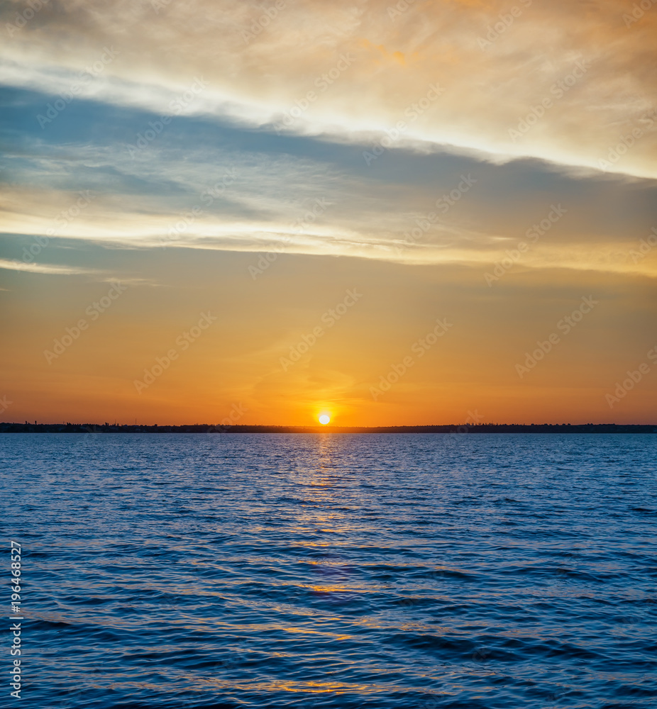 blue dark water in river and orange sunset in clouds