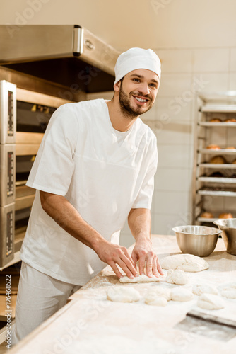 smiling young baker preparing raw dough at workplace on baking manufacture