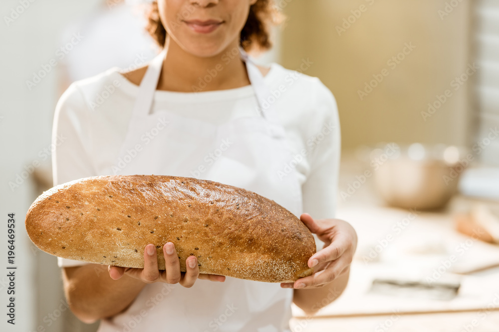 cropped shot of female baker holding fresh loaf of bread on baking manufacture cropped shot of female baker holding fresh loaf of bread on baking manufacture