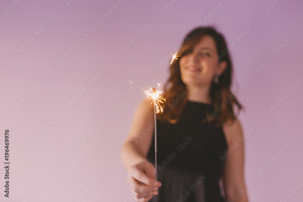 Obraz premium young beautiful woman having fun with sparkles indoors. Purple background. Casual clothing. Fun, happiness and lifestyle