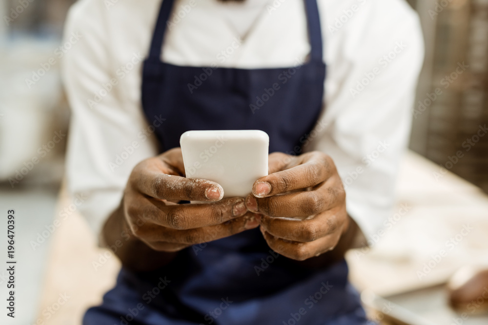 cropped shot of african american baker with hands covered in flour using smartphone cropped shot of african american baker with hands covered in flour using smartphone