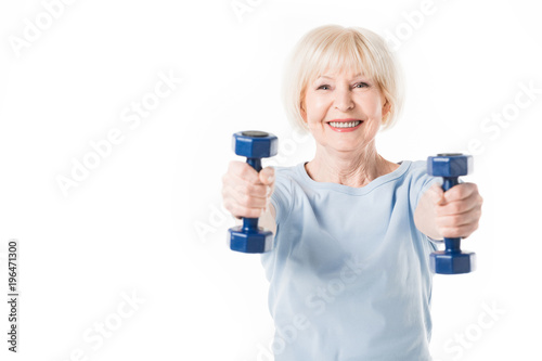 Smiling senior sportswoman with dumbbells in hands isolated on white