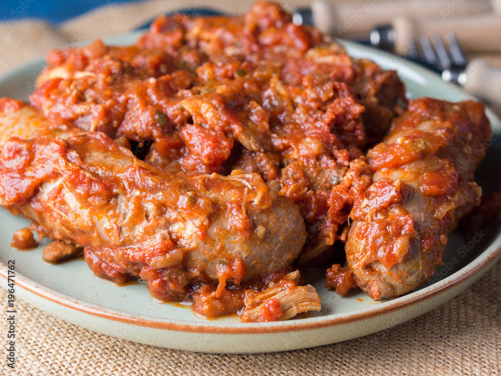 Sausages and pork pullet cooked in traditional Italian tomato ragu sauce. Dish on burlap with cutlery. Sausages and pork pullet cooked in traditional Italian tomato ragu sauce. Dish on burlap with cutlery.