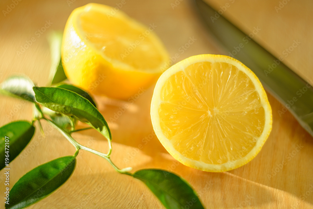 Cut lemon with green leaves and a knife on a wooden board lit by the sun Cut lemon with green leaves and a knife on a wooden board lit by the sun