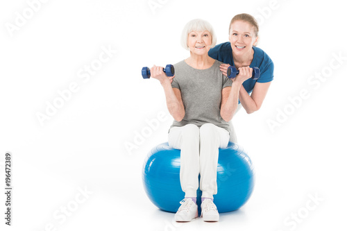 Portrait of coach and sportswoman with dumbbells and fitness ball isolated on white