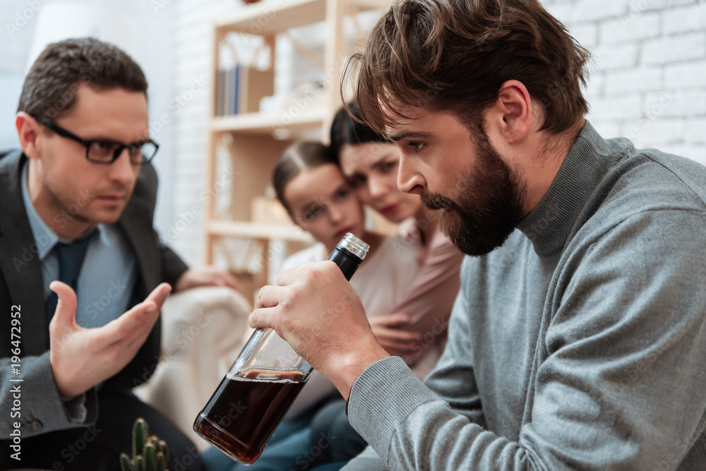 Anxious mother and daughter look at father of alcoholic sitting at reception with psychologist. Anxious mother and daughter look at father of alcoholic sitting at reception with psychologist.