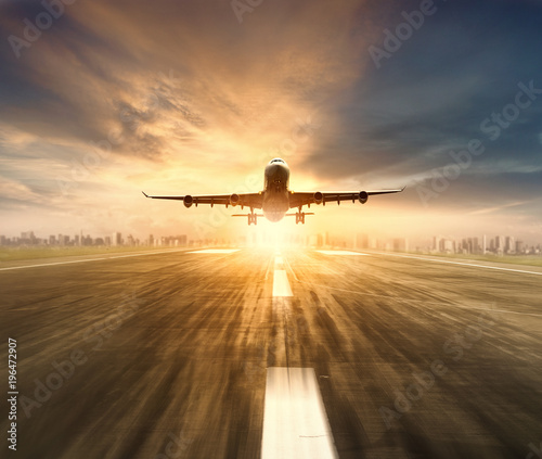 air plane flying over airport runway with city scape and sunset sky background