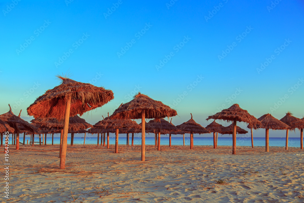 Straw umbrellas on the beach on a sunset.