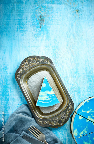 sliced cake and piece of mousse cake with blue glaze on a looking like silver, vintage metal dish on the white-blue wooden background © vitaliymateha