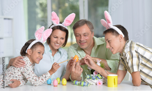 Happy family of four wearing bunny ears and painting Easter eggs