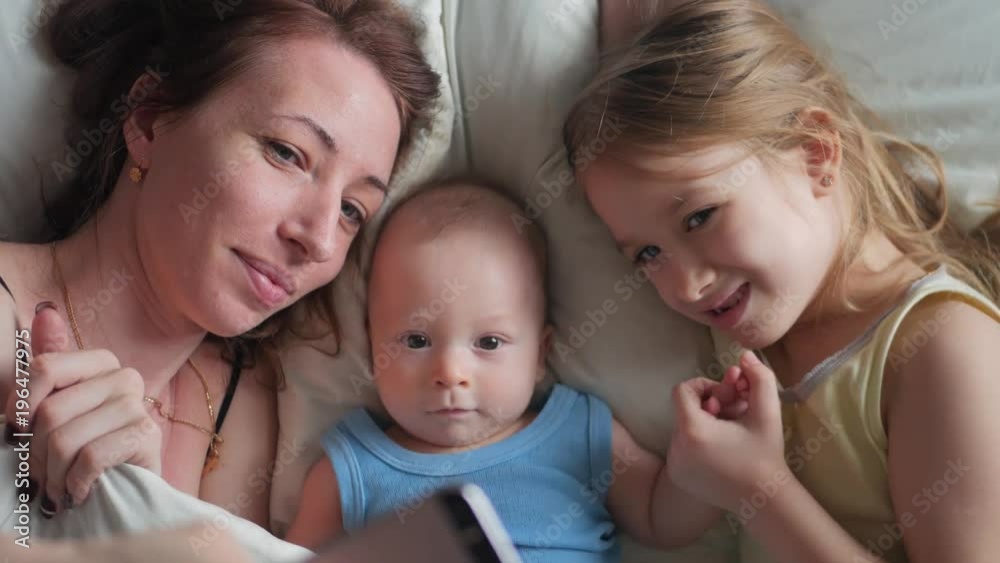 Happy mother and her young children taking selfie with smartphone on bed Happy mother and her young children taking selfie with smartphone on bed