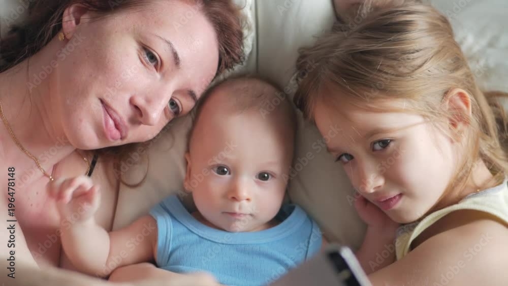Happy mother and her young children taking selfie with smartphone on bed Happy mother and her young children taking selfie with smartphone on bed