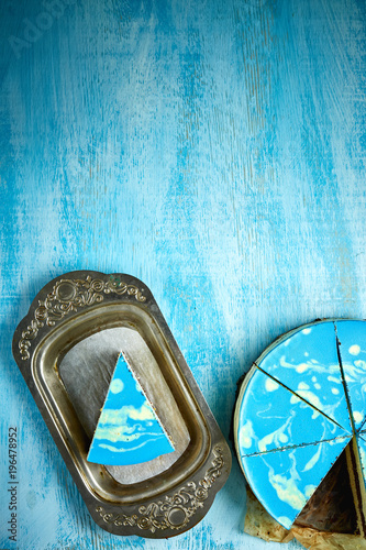 piece of mousse cake with blue glaze on a looking like silver, vintage metal dish on the white-blue wooden background © vitaliymateha