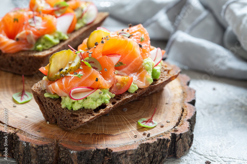Smorrebrod with salmon on rye bread with vegetables and herbs