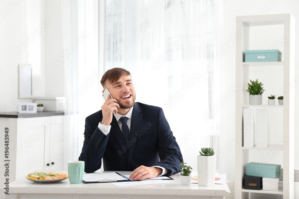 Young businessman talking on mobile phone while working in office Young businessman talking on mobile phone while working in office