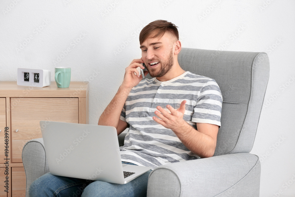 Young man talking on mobile phone while working with laptop at home Young man talking on mobile phone while working with laptop at home