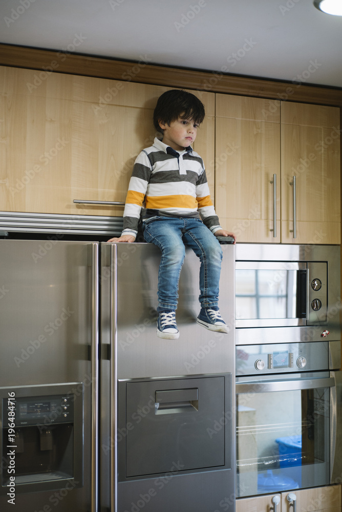 child is sitting above the fridge child is sitting above the fridge