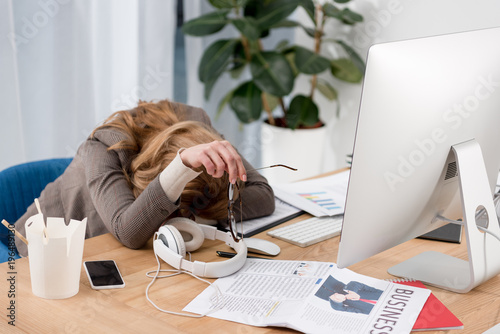 partial view of exhausted businesswoman sleeping at workplace with documents in office photo