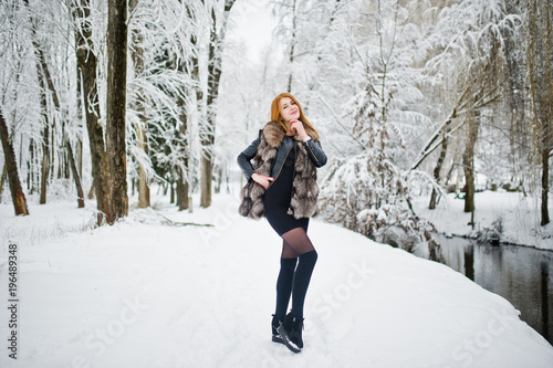 Red haired girl in fur coat walking at winter snowy park.