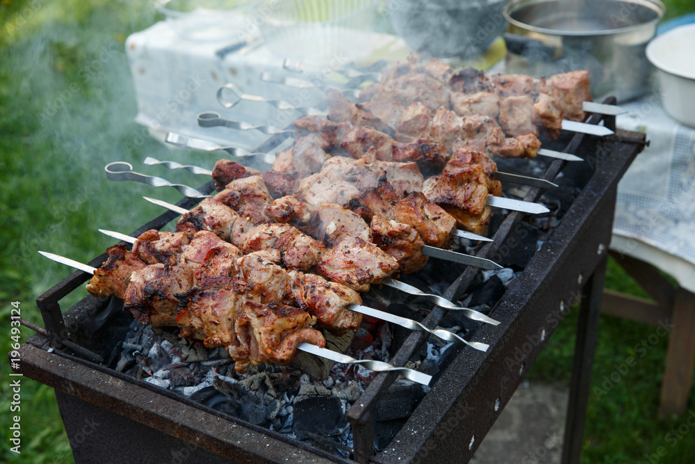Shashlik or shashlyk preparing on a barbecue grill over charcoal. Grilled cubes of pork meat on metal skewer. Outdoor.