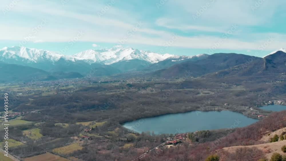 Aerial: drone panning over forest valley lake, aerial view of snow capped mountain range on the Alps, clear blue sky, Turin, Italy. Aerial: drone panning over forest valley lake, aerial view of snow capped mountain range on the Alps, clear blue sky, Turin, Italy.