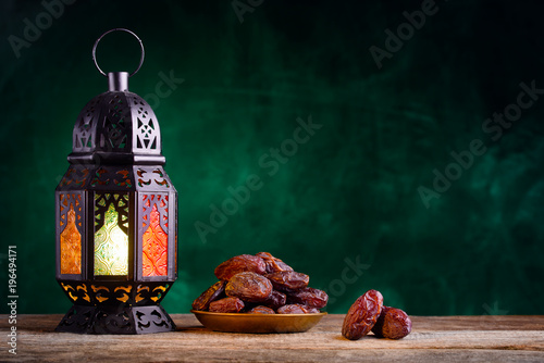 Ramadan concept. Dates close-up in the foreground. Ramadan Lantern on a wooden table. Textured green wall background. Space for text on the right. photo