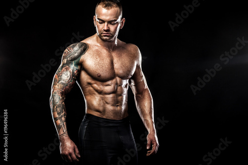 Handsome fit man posing wearing in jeans with tattoo. Sport and fashion concept isolated on black background.