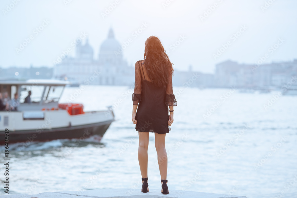 Obraz premium Travel tourist woman standing on the pier against beautiful view on venetian chanal with boats in Venice, Italy. Attractive young romantic girl on vacation walking happy by Grand Canal. Gorgeous mixed