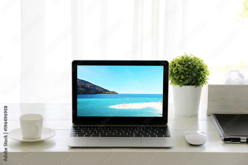 Beach in screen Laptop on table and Coffee cup room Office morning.concept of time relax. Beach in screen Laptop on table and Coffee cup room Office morning.concept of time relax.