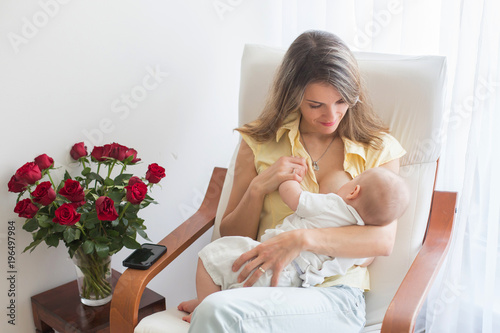 Young mother holding her baby boy, brestfeeding him, sitting in armchair photo